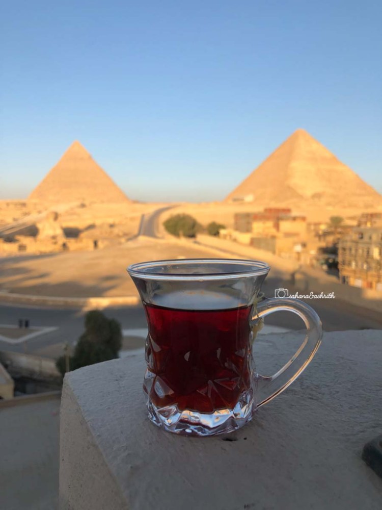 Hibiscus tea in a glass placed on a terrace's parapet with the view of Giza's pyramid.