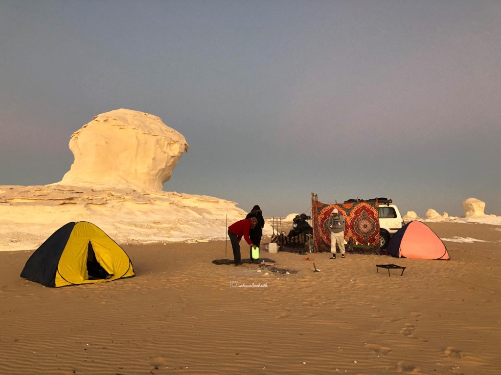 Tents setup in the middle of white desert beside a huge lime formation