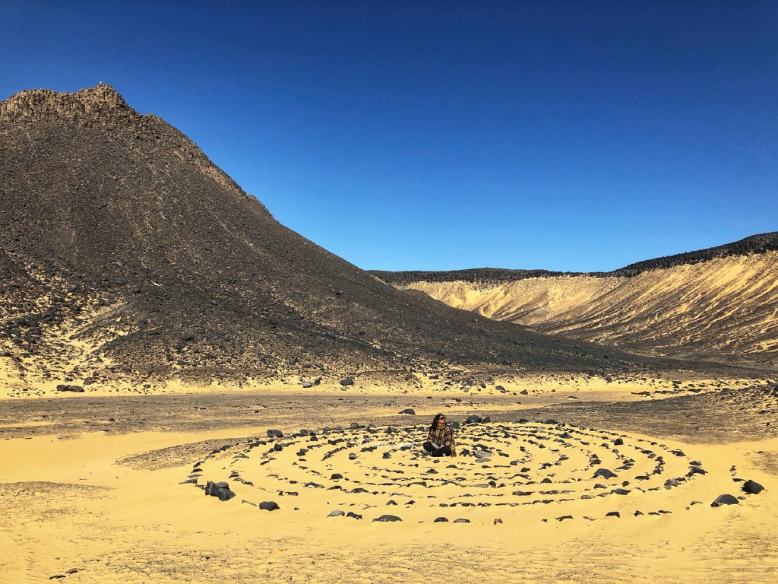 Indian traveller sitting in the centre of Concurrent circles made of black stones in brown desert