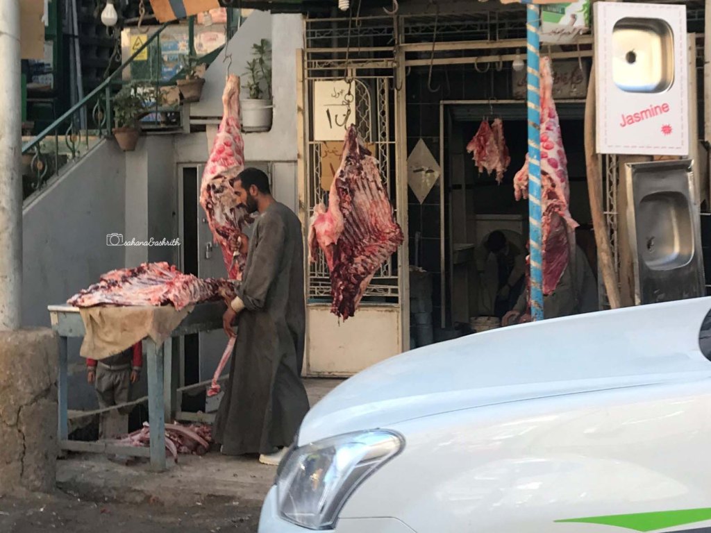 Egyptian butcher wearing Jalebiya chopping and meat hung open by the sdusty street side