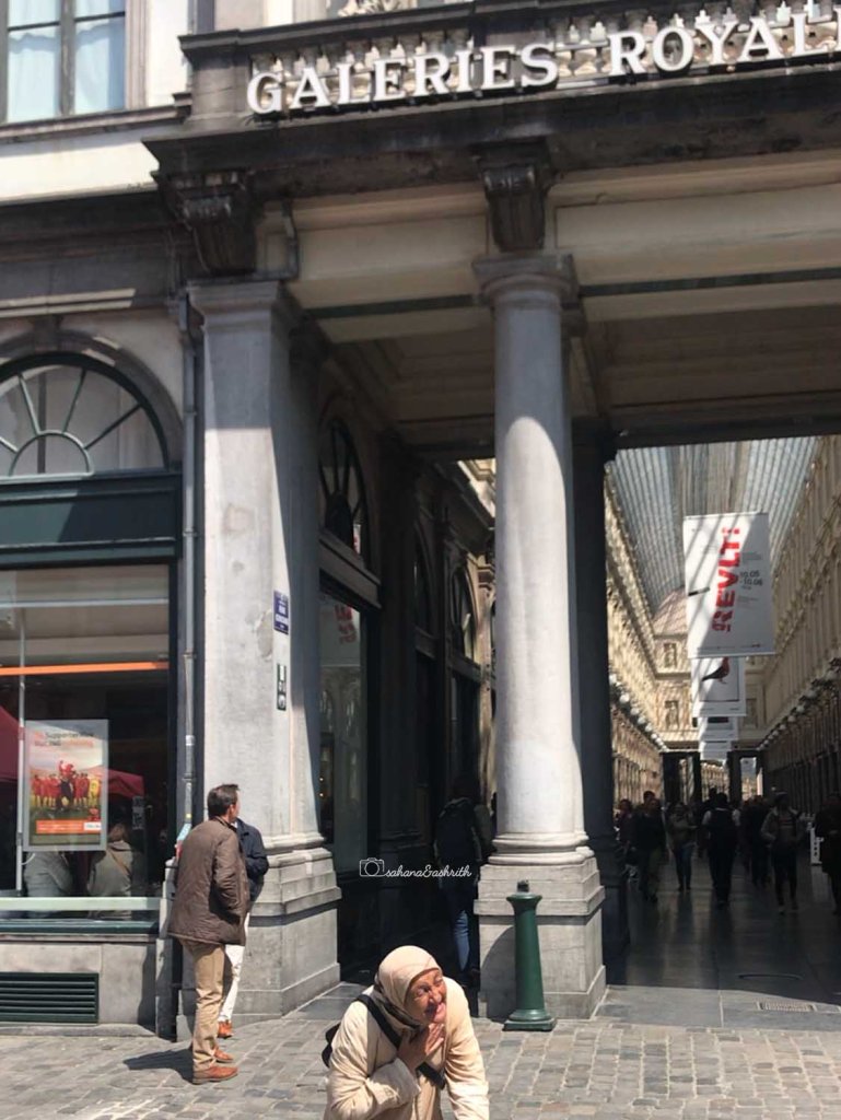 Old woman begging in front of luxury shopping aracade Royal gallery pf Saint Hubert in Brussels