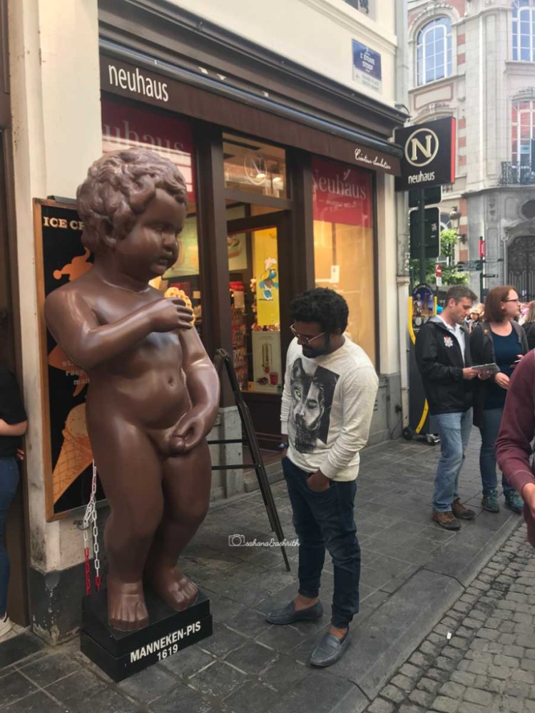 Indian traveller looking at a giant replica of mannekin pis eating waffles at Brussels
