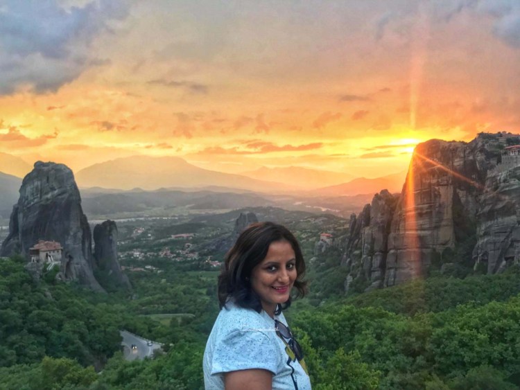 most beautiful sunset at Meteora with greyish clouds and glowing sun and rays penetrating between tall mountains and meteora monasteries
