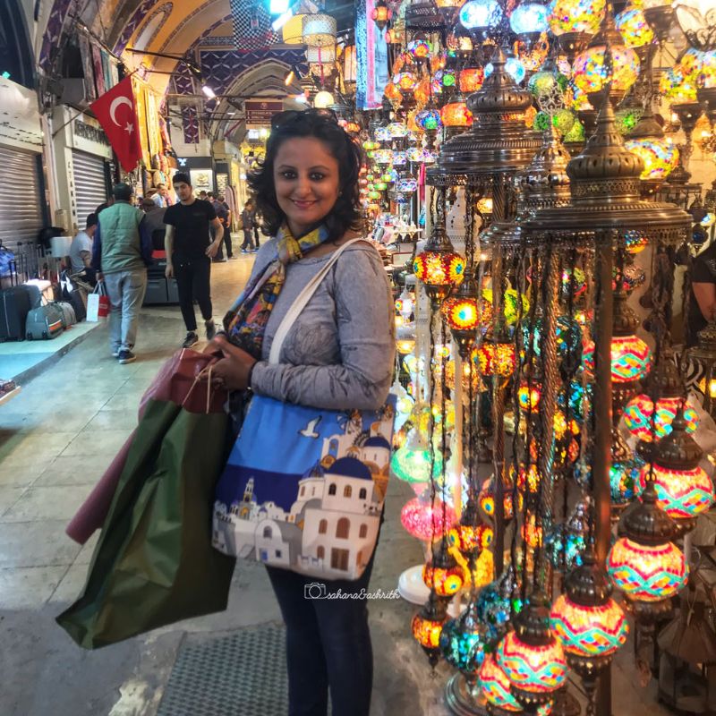 Indian traveller standing infrotnt of a shop of colourful turkish lamps