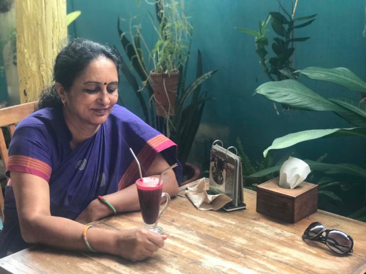 indian woman in purple cotton saree sitting at a vegan cafe looking at beetroot shake