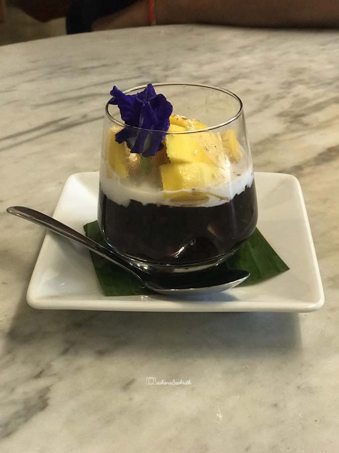 mango sticky rice served in a small bowl along with a blue flower on top of mango chunks