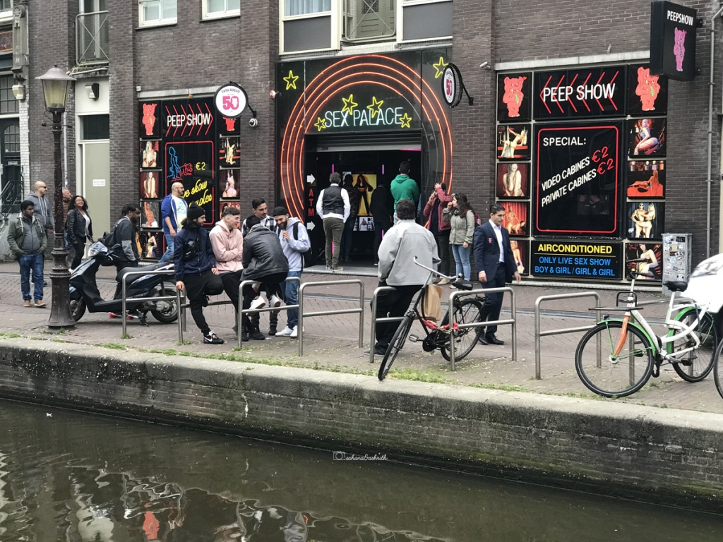 Cycles parked and People waiting at Red light district of Amsterdam in front of a building that says "Sex Palace"