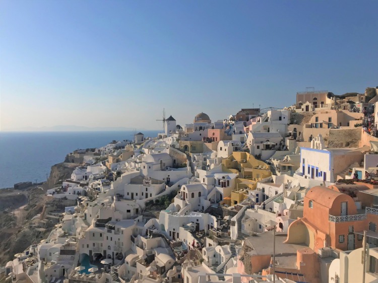 Cube white houses and a few windmills stacked along the terrain of Oia in Santorini by the seaside