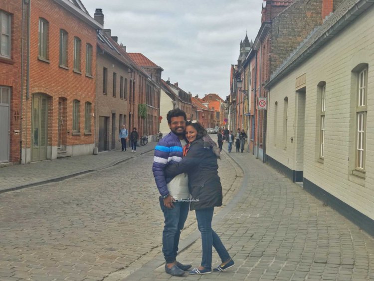 Indian couple travellers hugging each other at Brugges walkway filled with beautiful renaissance buildings on either side 