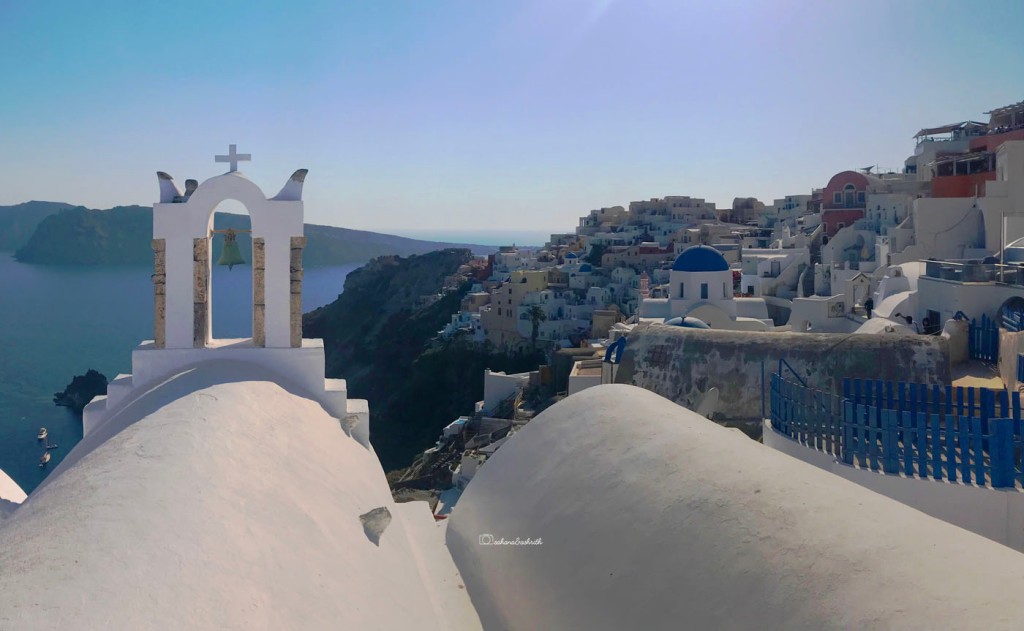 View of sea through vaulted church roof beside the terraced town of Oia full of white cube houses and blue dome