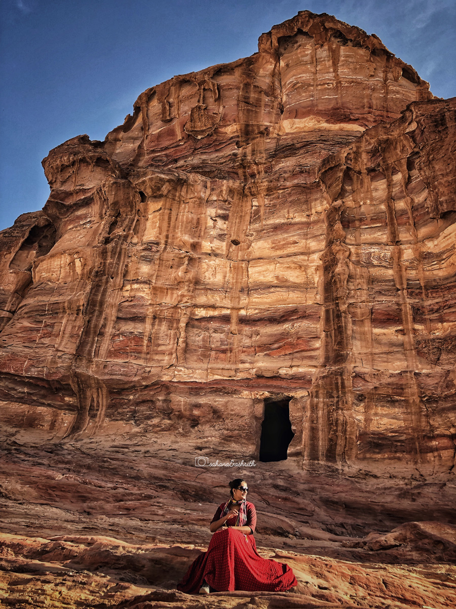 Girl in red gown sitting infront of  a Petra cave