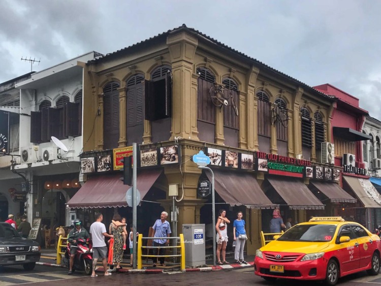 old Phuket coffee shop with brown facade and a yelow taxi passing by