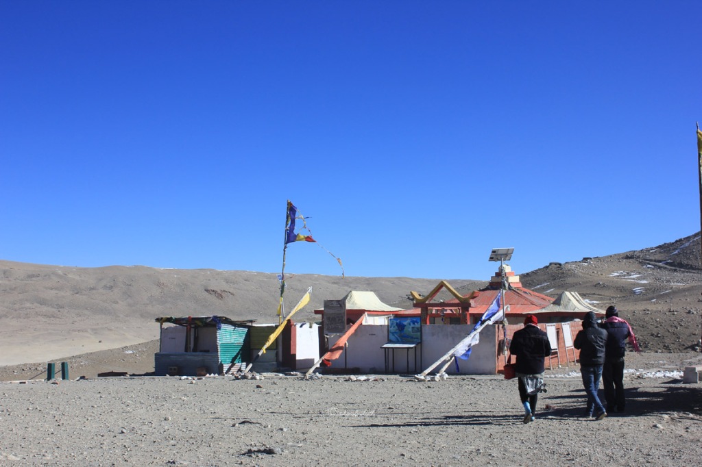 Small temple with Buddhist flags waving in the middle of the desert near lake