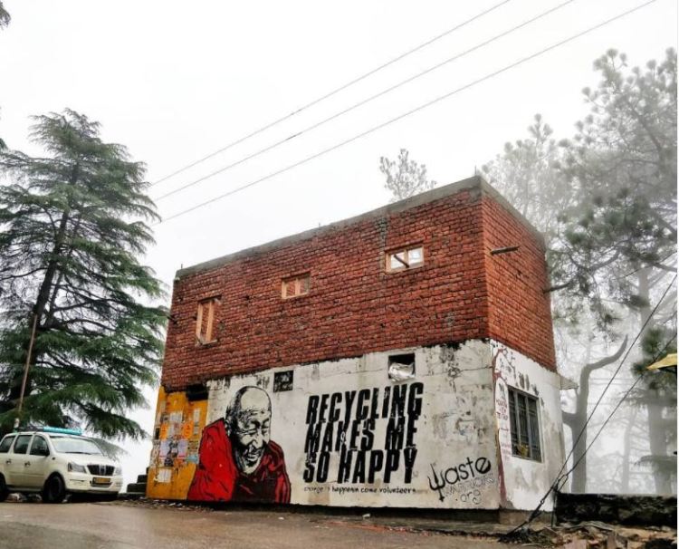 Worn out brick building at Dharmashaala with grafitti that says recycling makes me happy.