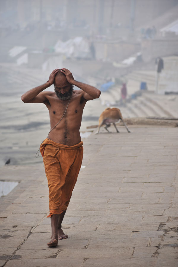 A priest wearing saffron robe walking on the ghats barechested after taking a dip in the freezing cold water of river Ganga at Banaras