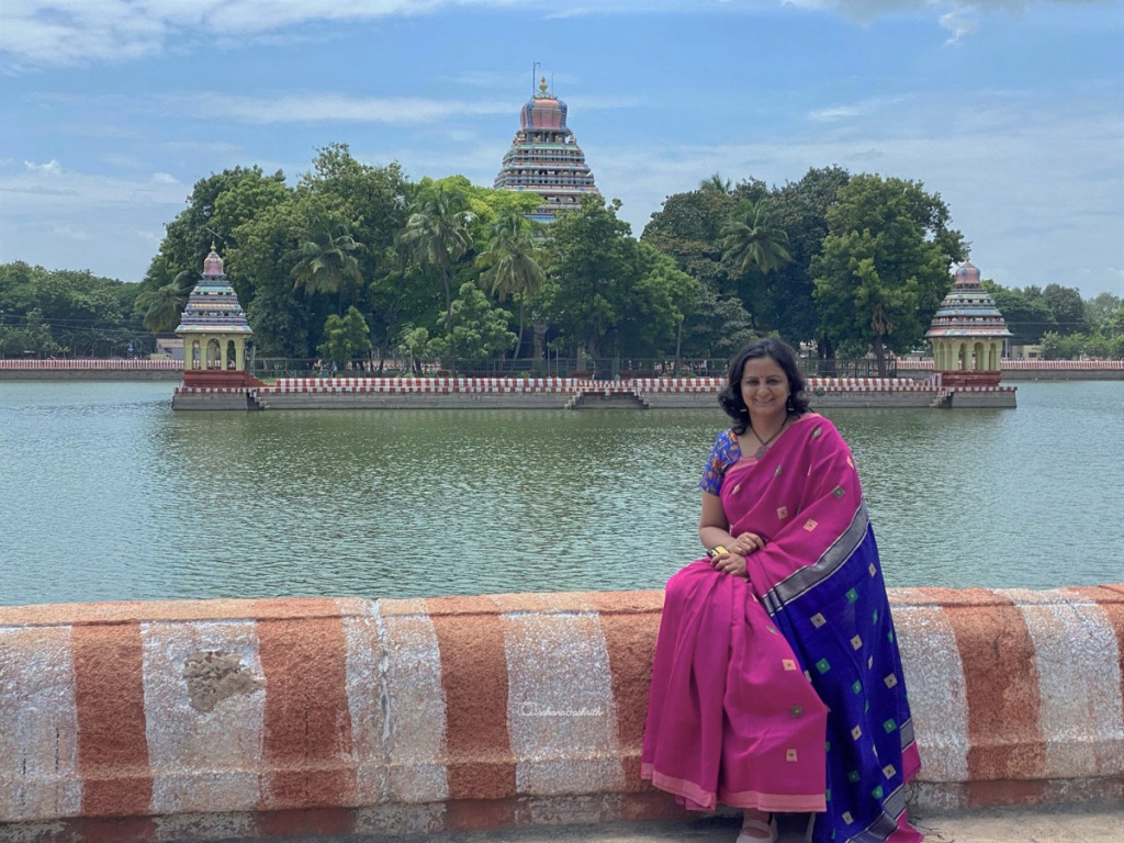 Beautiful typical south Indian temple on the lake and a lady wearing saree posing in front of it.