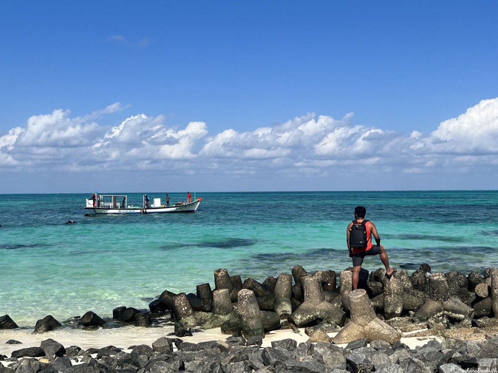 Man waiting on rocks watching a boat pass by on blue water in Lakshadweep